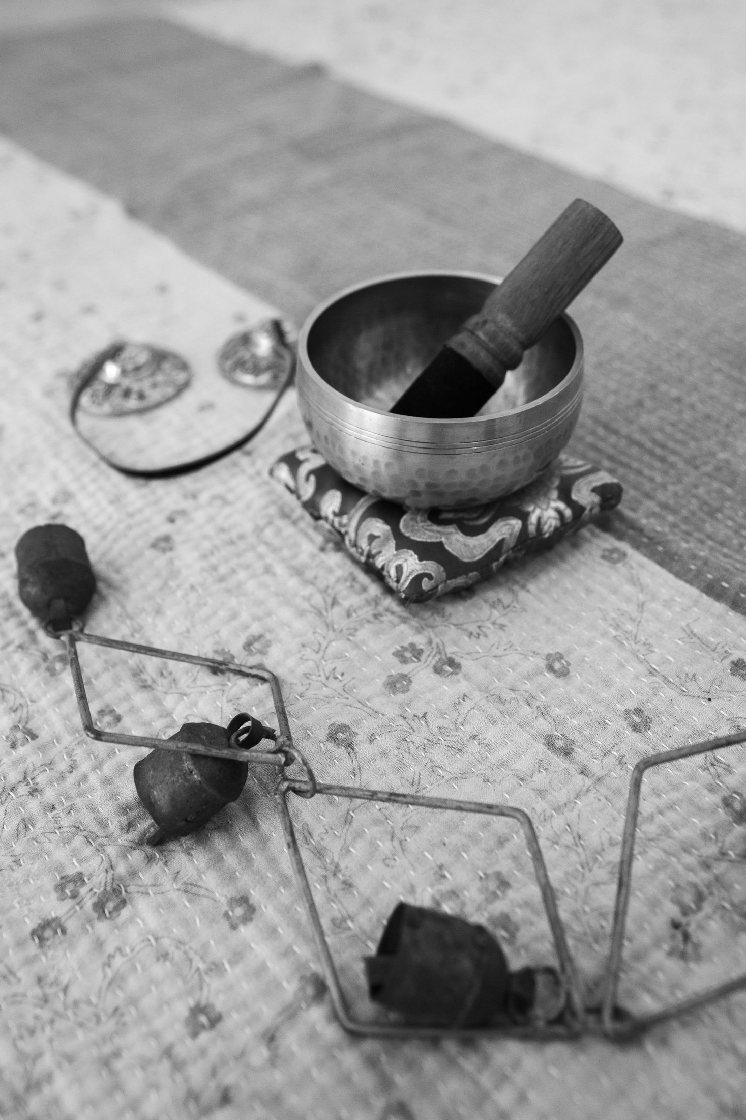 A small singing bowl and bells resting on a quilted mat.