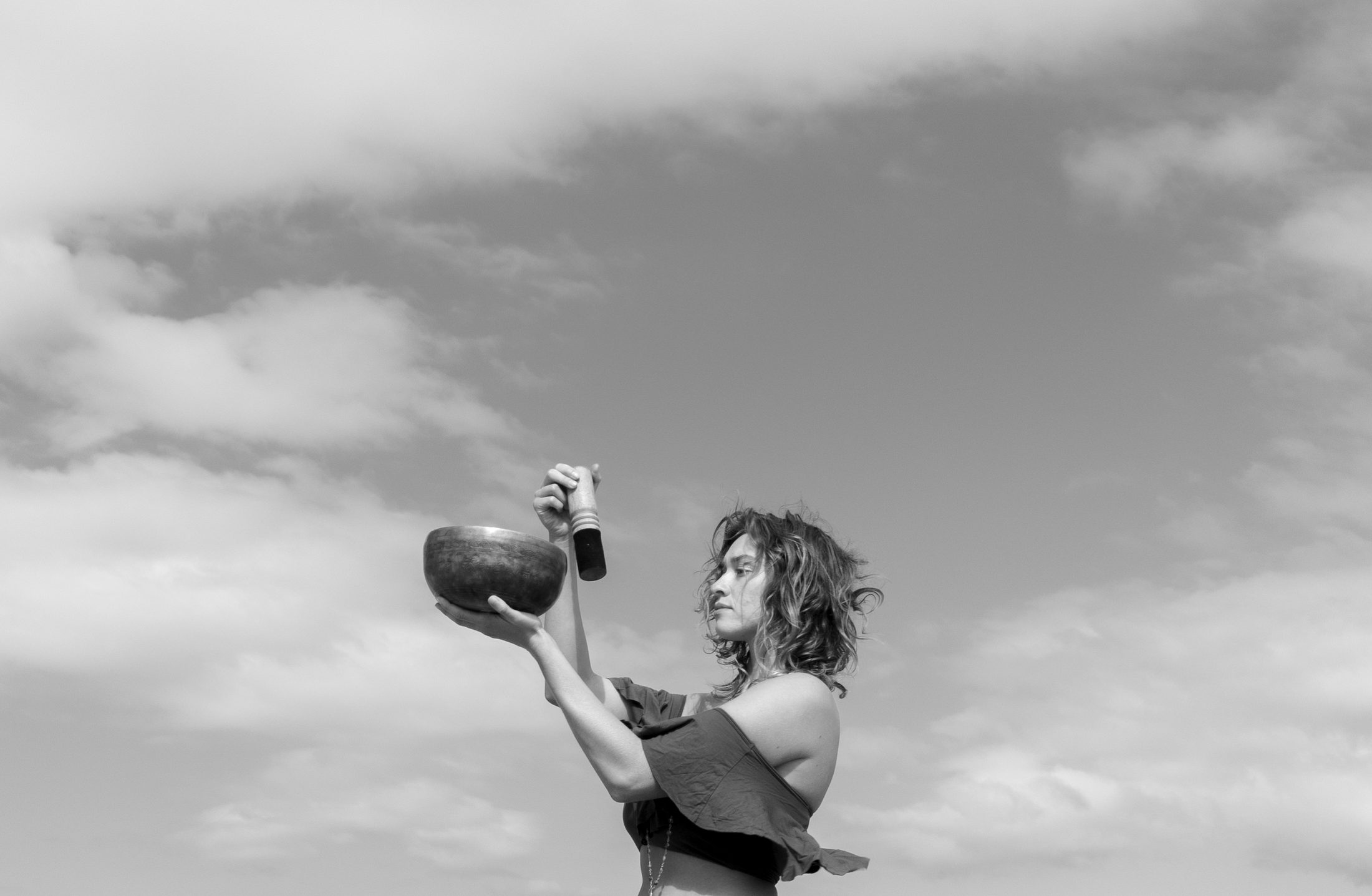 Riley raising a singing bowl against an open sky.